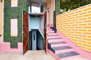 Una escalera conduce a un área de recepción con un letrero, rodeada de paredes con follaje verde y un diseño de ladrillo amarillo.