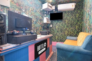 Quarto de hotel com televisão, aparelhos de ar condicionado, escrivaninha com computador e sofá.