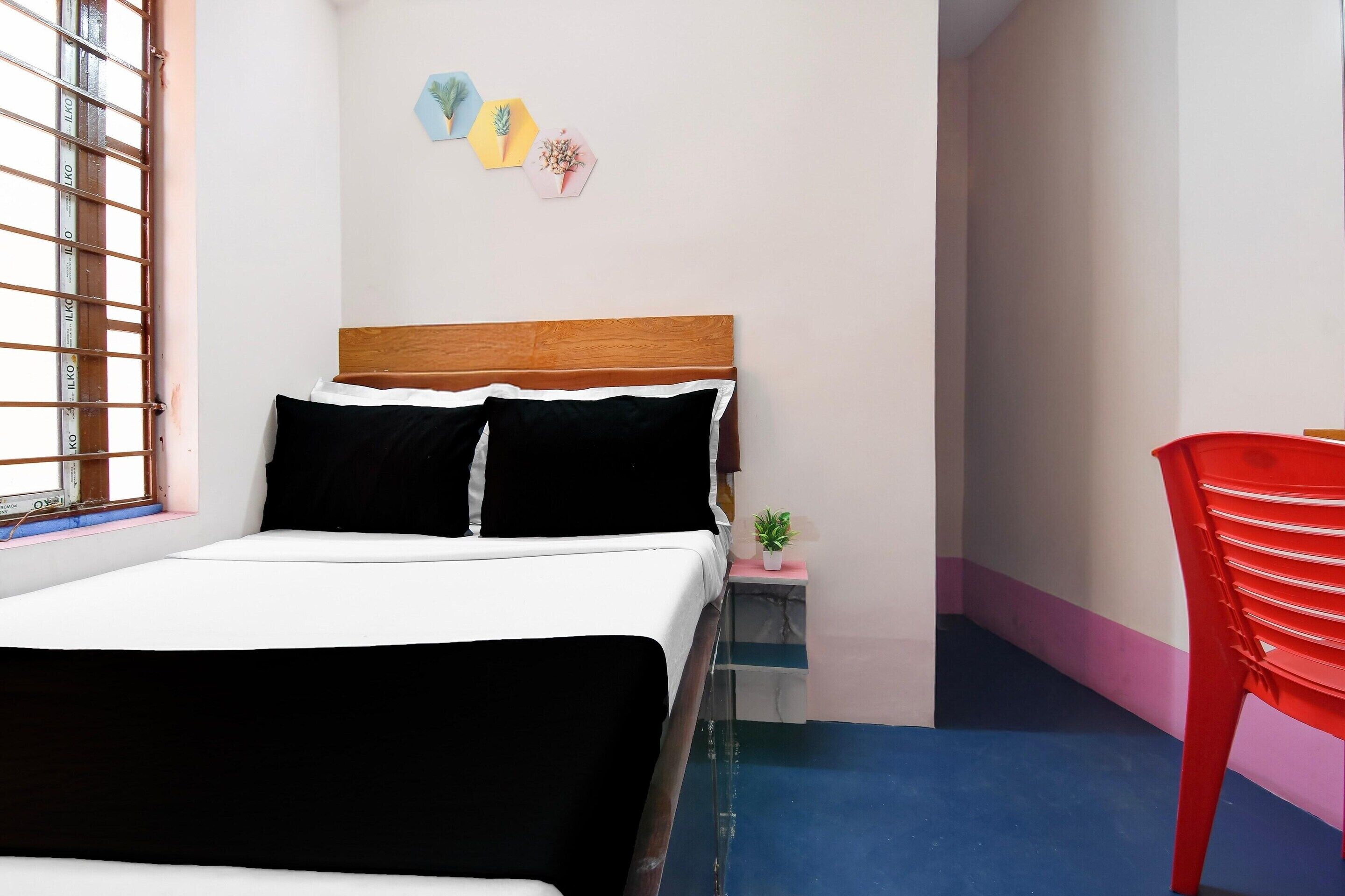Un dormitorio con cama, una mesita de noche con una planta, una silla roja y una ventana con barrotes.
