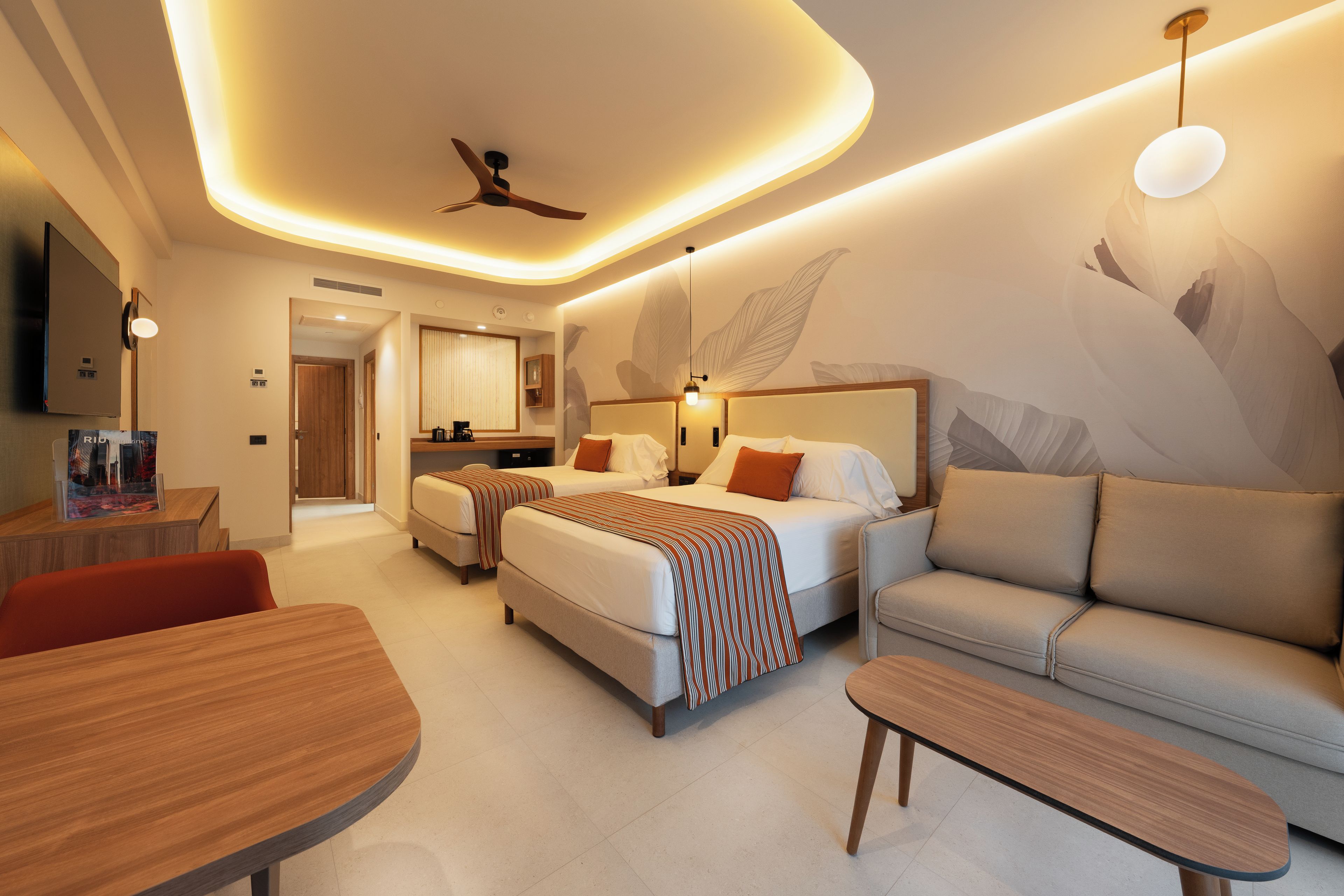 A modern hotel room with a bed, sofa, and a dining area.