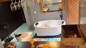 A room with a bathtub, a wooden table with snacks and drinks, and a mirror on the wall.