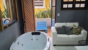 A modern bathroom with a freestanding bathtub, a white sofa with cushions, and a blue bench outside.