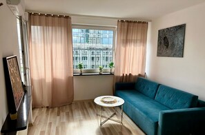 Una sala de estar con sofá, una mesita redonda y una ventana con cortinas.
