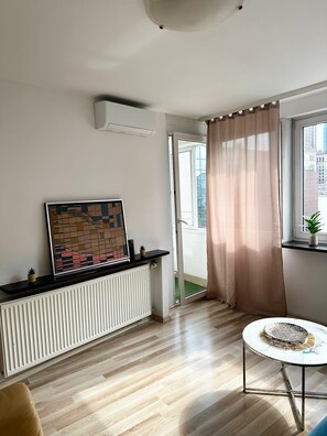 A modern living room with a radiator, a painting, a potted plant, and a view of the outside. - Warsaw Core 3-bedrooms apartment in City Center, Pet Friendly (Warszawa)