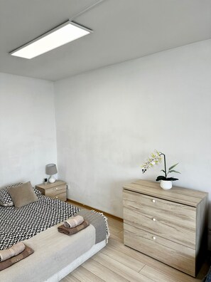 A minimalist bedroom with a bed, a nightstand, a dresser, and a potted orchid. - Warsaw Core 3-bedrooms apartment in City Center, Pet Friendly (Warszawa)