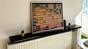 Ett rum med ett element, en svart hylla med en dekorativ prydnad och ett fönster med utsikt.