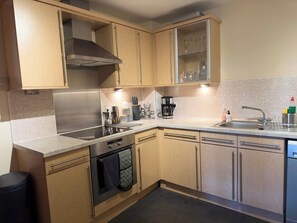 A modern kitchen with stainless steel appliances, wooden cabinets, and a tiled backsplash. - Our apartment is close to the City Centre and Leith (Edinburgh)