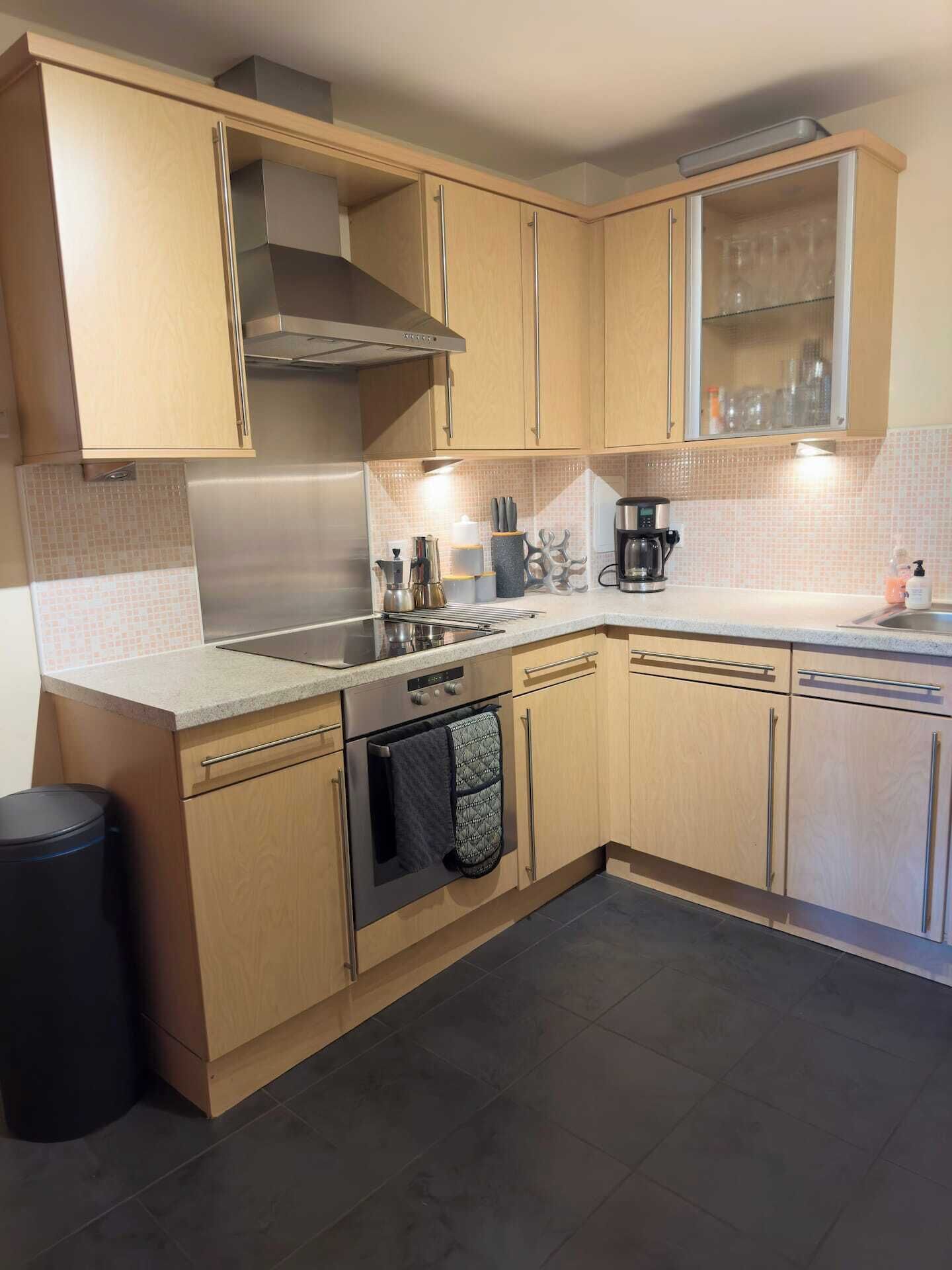 A modern kitchen with light wood cabinets, stainless steel appliances, and a tiled backsplash.