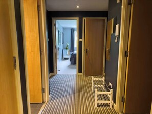 A hotel hallway with a striped carpet, wooden doors, and a view into a room with a bed and a plant. - Our apartment is close to the City Centre and Leith (Edinburgh)