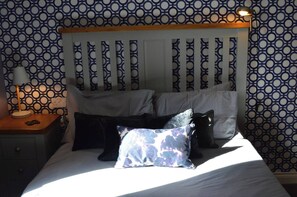 A bed with a wooden headboard, a bedside lamp, and patterned wallpaper. - Our apartment is close to the City Centre and Leith (Edinburgh)