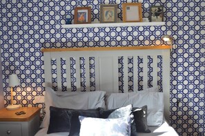 A bedroom with a patterned wallpaper, a wooden headboard, a bedside table with a lamp, and a nightstand. - Our apartment is close to the City Centre and Leith (Edinburgh)