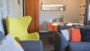 Ein Wohnzimmer mit einem grünen Sessel, einem blauen Sofa mit Kissen, einer Holztür, einem weißen Tisch und einem Spiegel an der Wand.