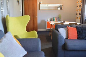A living room with a green chair, a blue sofa with pillows, a wooden door, a white table, and a mirror on the wall. - Our apartment is close to the City Centre and Leith (Edinburgh)