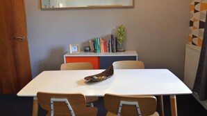 Ein Konferenzraum mit einem weißen Tisch, zwei Stühlen, einem Bücherregal mit Büchern, einem gerahmten Bild und einer Topfpflanze.