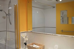 Ein Badezimmer mit Duschkabine aus Glas, einer gelben Akzentwand und einem Spiegel mit Handtuchhalter.