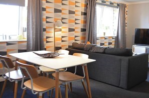 A modern living room with a sofa, a dining table with chairs, a flat-screen TV, and a patterned wall. - Our apartment is close to the City Centre and Leith (Edinburgh)
