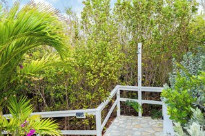 A white wooden staircase leading up to a covered area surrounded by lush greenery and various plants. - Island Studio with Pool Access, Porch & Workspace (Venetian Road Settlement)