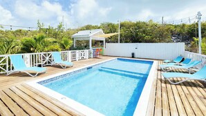A pool area with a wooden deck, lounge chairs, and a covered seating area. - Island Studio with Pool Access, Porch & Workspace (Venetian Road Settlement)