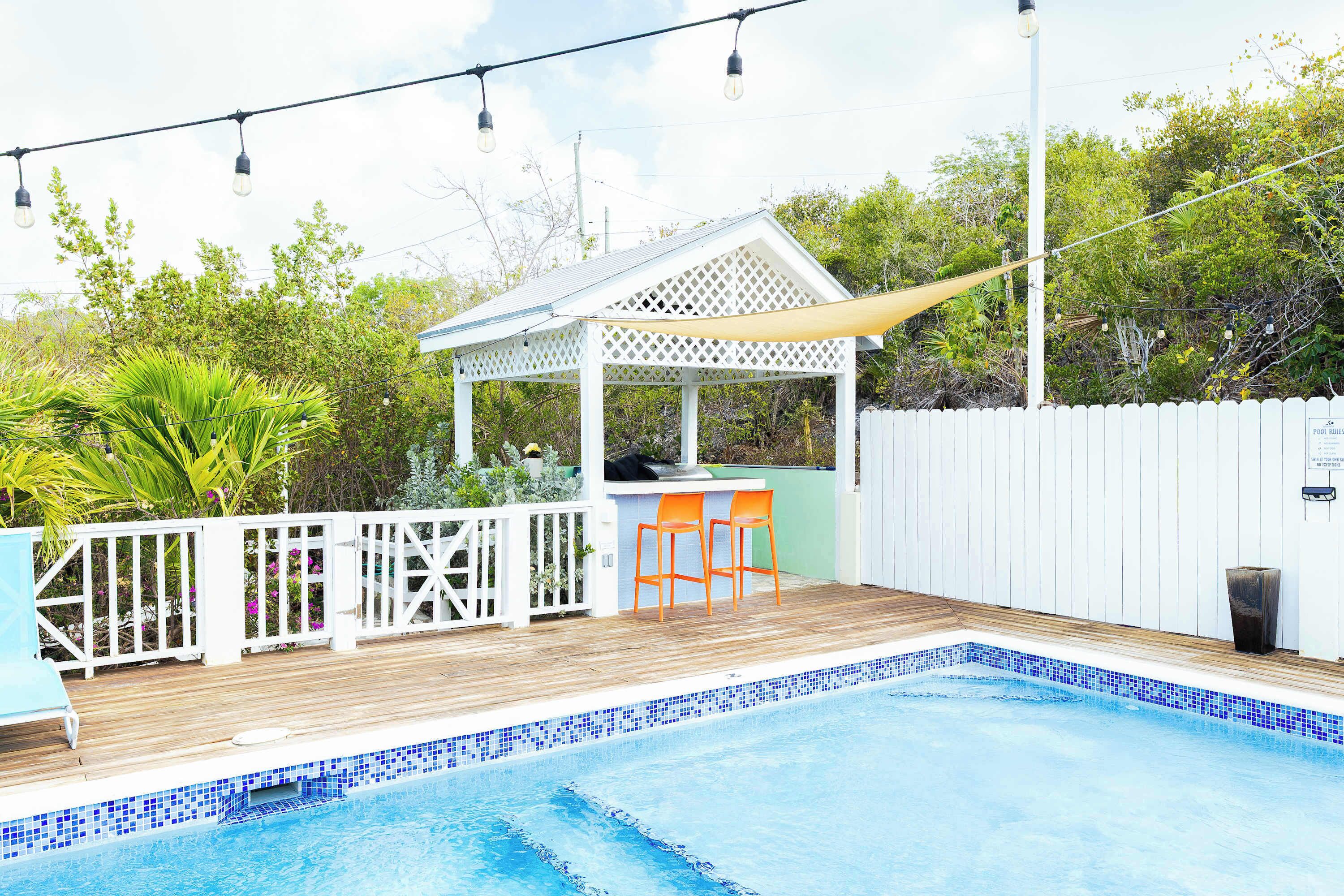 A swimming pool with a wooden deck, a gazebo, and a white fence.