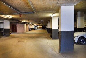 An underground parking garage with concrete pillars, a white car parked, and a brick wall. - Luxury boutique apartment decorated to a high standard (Edinburgh)