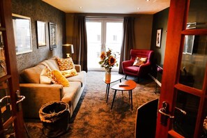 Ein Wohnzimmer mit einer Couch, einem roten Sessel, einem Couchtisch und einer Vase mit Blumen.