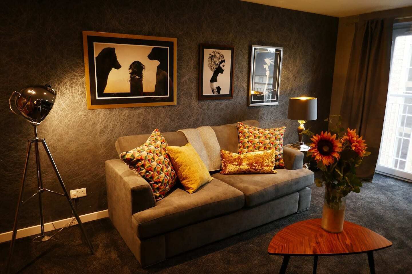 A living room with a sofa, patterned cushions, a floor lamp, and framed artwork on the wall.