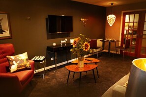 A living room with a sofa, a coffee table with a vase of flowers, a TV mounted on the wall, and a dining area with chairs and a table. - Luxury boutique apartment decorated to a high standard (Edinburgh)