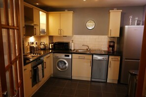 A compact kitchen with a washing machine, dishwasher, and a clock on the wall. - Luxury boutique apartment decorated to a high standard (Edinburgh)
