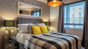 A hotel room with a large bed, a mirror above the bed, a nightstand with a lamp, and a window with curtains. - Boutique apartment newly decorated (Edinburgh)