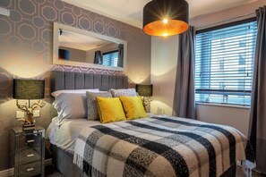 Ein Hotelzimmer mit einem großen Bett, einem Spiegel darüber, einem Nachttisch mit Lampe und einem Fenster mit Vorhängen.