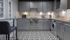 A modern kitchen with grey cabinets, a built-in oven, a washing machine, and a patterned floor. - Boutique apartment newly decorated (Edinburgh)