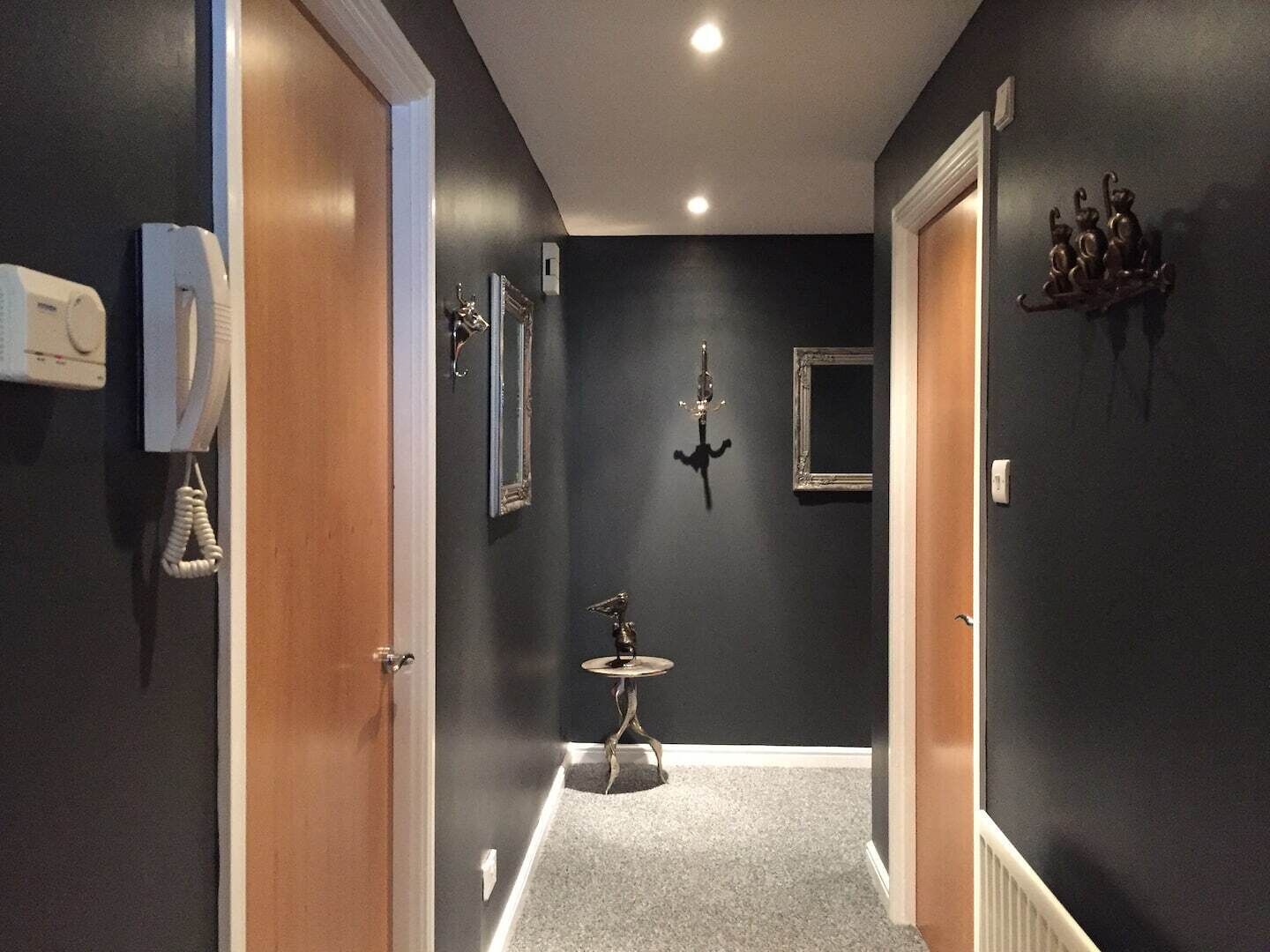 A hallway with a telephone, a coat rack, a small table, and a mirror on the wall.