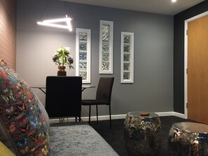 A modern living room with a grey wall, a dining table with chairs, a sofa with colorful cushions, and a decorative plant. - Boutique apartment newly decorated (Edinburgh)