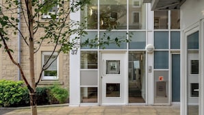 A building entrance with a glass door, a visible fire alarm, and a sign indicating a dry riser inlet. - Boutique apartment newly decorated (Edinburgh)