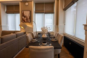 A dining area with a table set for four, flanked by two sofas, a floor lamp, and a vase with flowers. - Grand Leith Luxe: Jacuzzi & Cinema Room (Edinburgh)