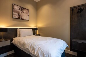 A hotel room with a large bed, two bedside tables, a wall-mounted artwork, and a wardrobe with hanging items. - Sophisticated Urban Living| Sleek 4-Bedroom Home (Edinburgh)