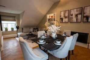 A dining area with a dark table set for four, light grey upholstered chairs, and a vase of white flowers. - Sophisticated Urban Living| Sleek 4-Bedroom Home (Edinburgh)