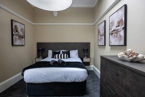 Ein Hotelzimmer mit einem großen Bett, zwei Nachttischen mit Lampen, einer Kommode und abstrakten Kunstwerken an den Wänden.