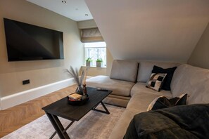 A modern living room with a sectional sofa, a flat-screen TV mounted on the wall, and a small table with decorative items. - Sophisticated Urban Living| Sleek 4-Bedroom Home (Edinburgh)