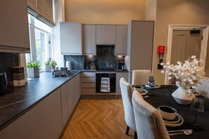 A modern kitchen with integrated appliances, a dining area with a table set for two, and a view of the adjacent living space. - Sophisticated Urban Living| Sleek 4-Bedroom Home (Edinburgh)