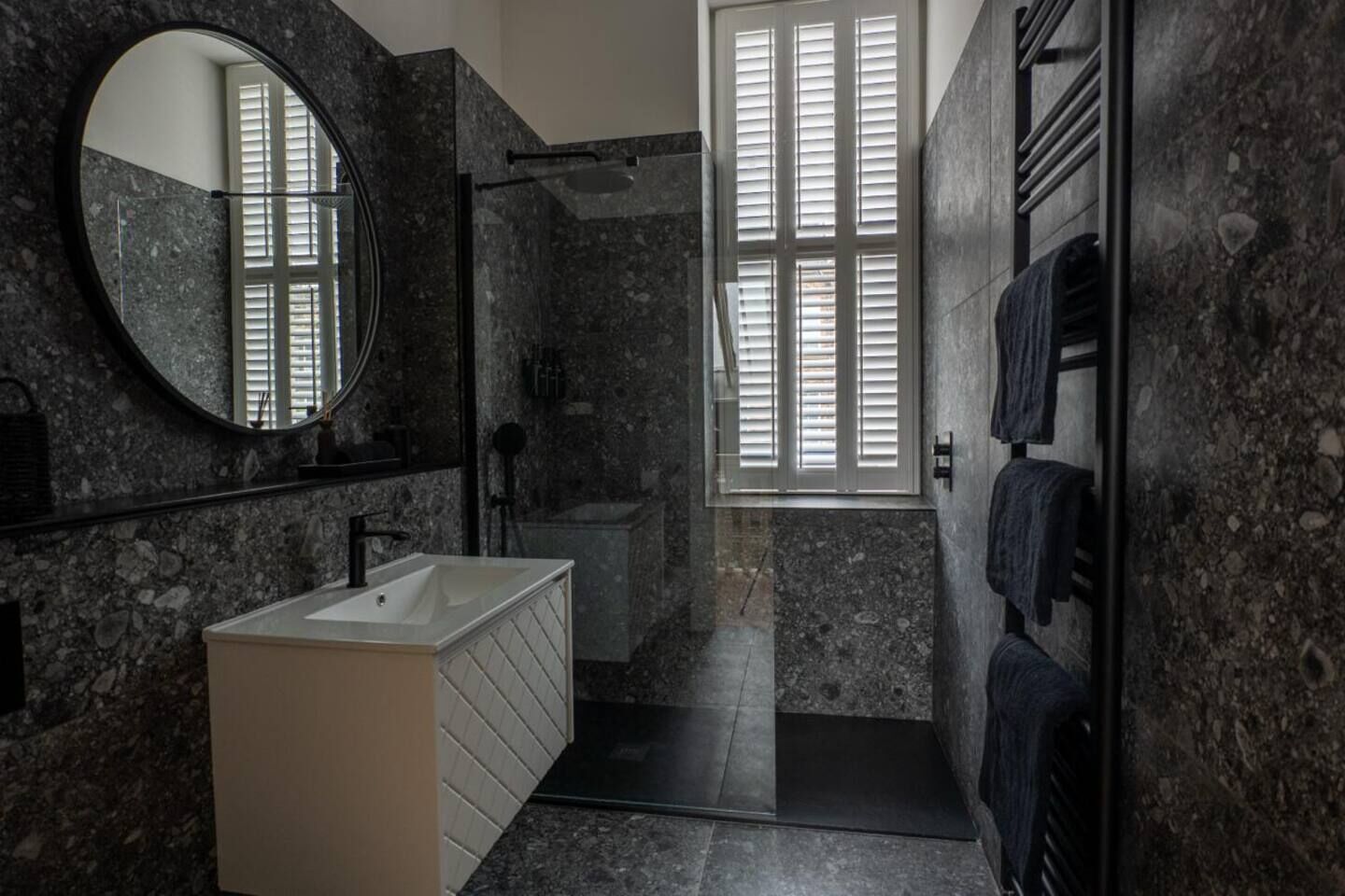 A bathroom with a marble sink, a mirror, a window with blinds, and a towel rack.