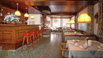 Een restaurant met een houten bar en zithoek, een vloer met patroon en hangende lampen.