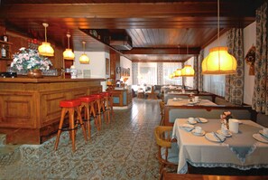A restaurant with wooden bar and seating area, patterned floor, and hanging lamps.