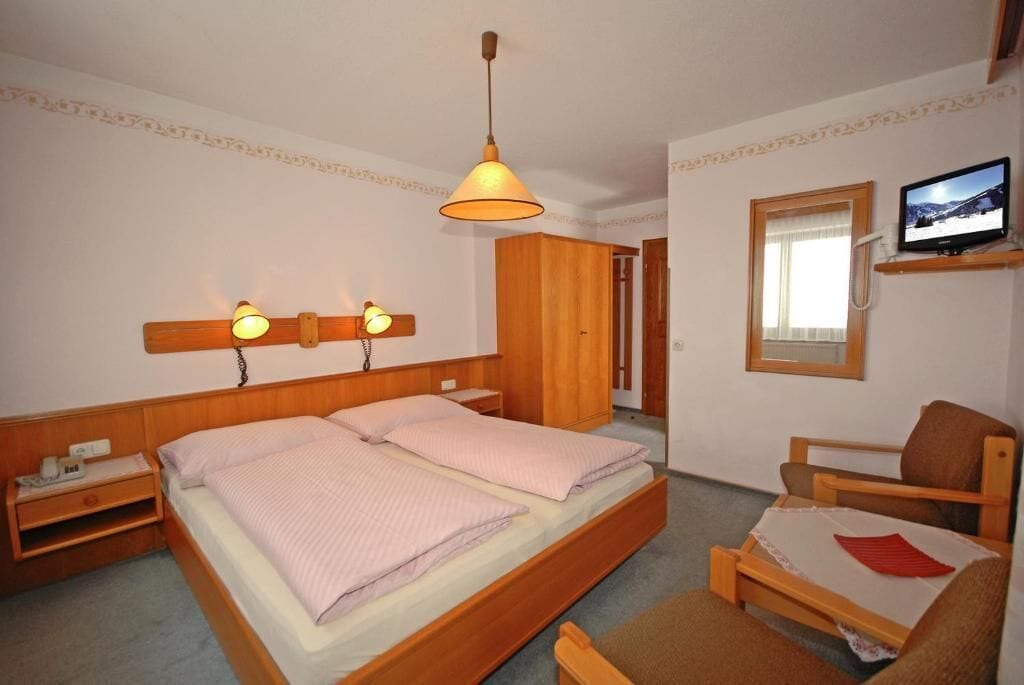 Een hotelkamer met een tweepersoonsbed, nachtlampjes, een televisie op een plank en een houten garderobe.