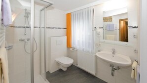 A bathroom with a glass shower enclosure, a toilet, a sink, and a mirror.