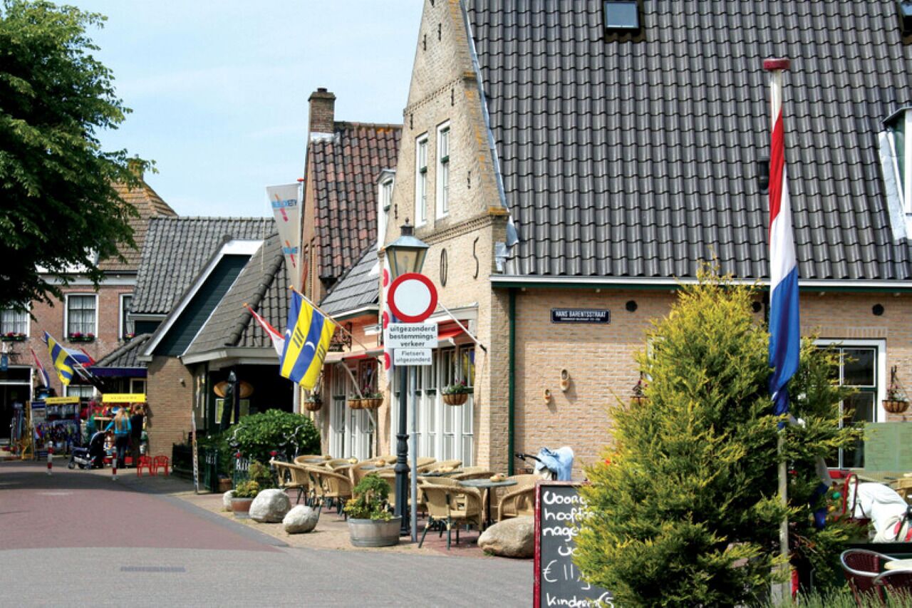 Una calle con edificios, mesas al aire libre y banderas.