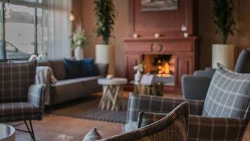 A cozy living room with a fireplace, sofas, and potted plants.