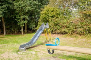 A playground with a slide and swings in a park. - 2 Comfy Rooms on Scenic Ameland – Near Beach, Ferry, Dunes & Cycling Routes (Nes)