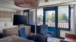 Een moderne hotelkamer met een groot bed, een flatscreen televisie, een zithoek met stoelen, en grote ramen met uitzicht op het buiten.