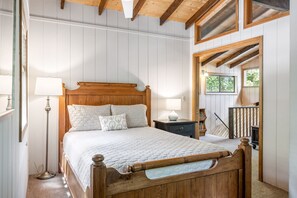 A bedroom with a wooden bed, bedside lamps, a nightstand, and a view of the outdoors through a window. - Lakeside Getaway at Innsbrook by Sarah Bernard (Innsbrook)